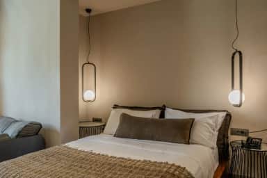 Junior Suite bed with white linen and brown cushions between two oval pendant lamps