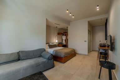 Junior Suite seating area with a grey sofa, the double bed beyond, a wall TV and a desk