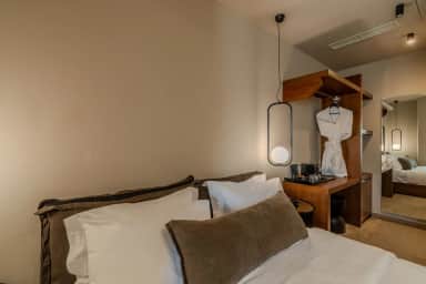 Junior Suite bed with white pillows, a pendant lamp and an open wooden wardrobe with a white bathrobe