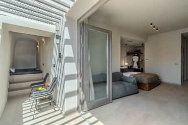 Junior Suite veranda in striped pergola shade, two chairs and a small table, glass doors open to the bedroom