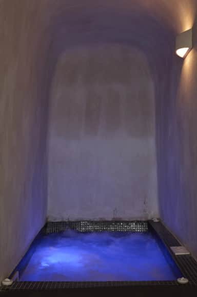 Junior Suite heated jacuzzi lit violet blue in a whitewashed cave-style vault, its water churning below a wall lamp