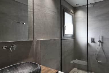 Superior Double Room bathroom with a dark stone vessel basin, grey textured tiles and a glass walk-in shower with a rain head