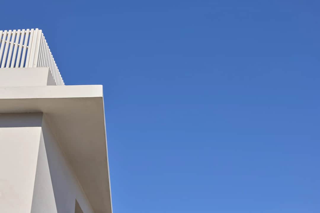White roof overhang and slatted rooftop parapet at one corner of the building, set against a wide clear blue sky