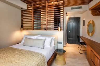 Double bed under a wooden slatted screen with gold pendant lights, a desk and a round mirror by the door