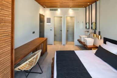 Long view of the room with a wooden desk and rattan chair, twin basins by the bed and two doorways at the end