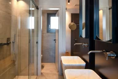 Bathroom with a glass shower, twin white stone basins under dark-framed mirrors and a separate toilet room