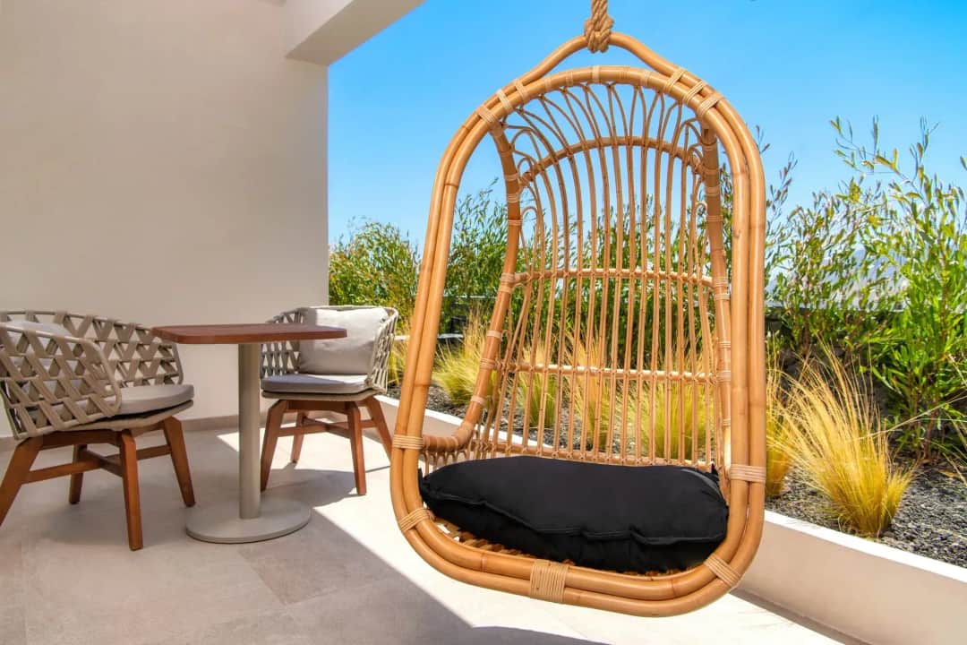 Hanging rattan chair and a small table for two on a sunny terrace lined with plants