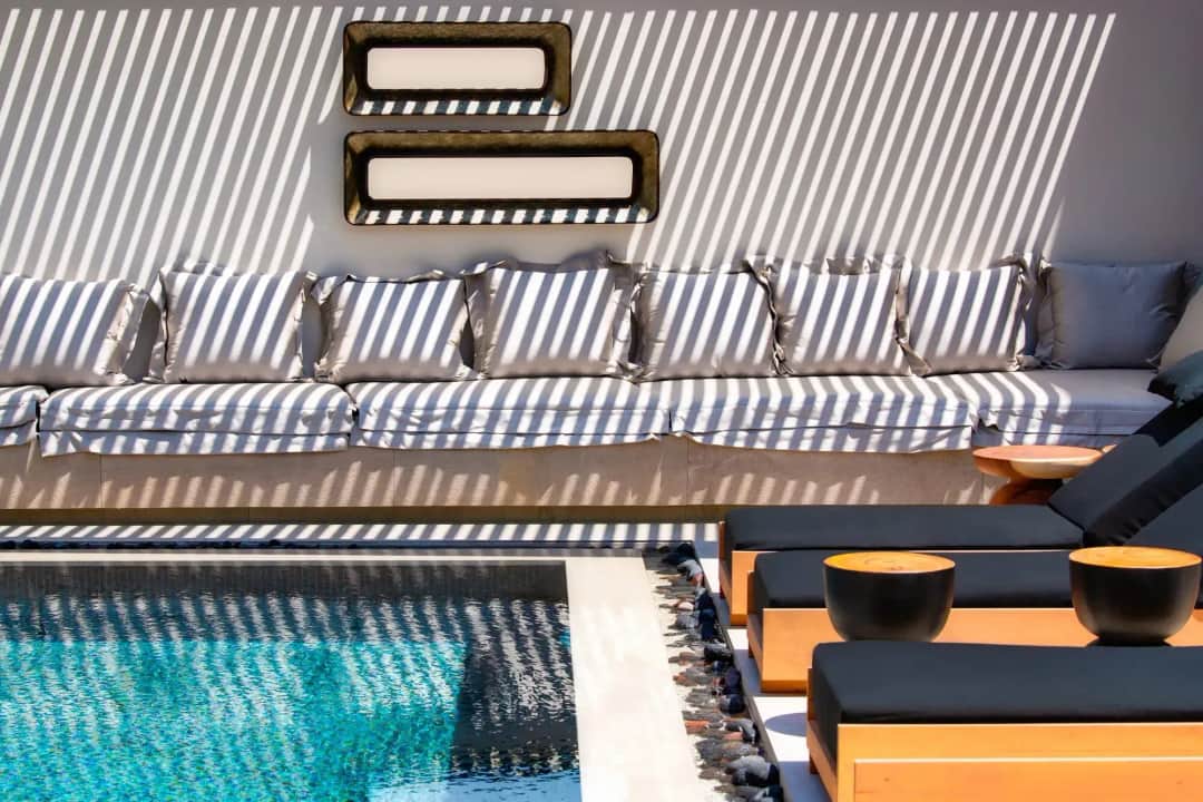 Shaded poolside lounge with striped cushions on a built-in sofa, sunbeds beside the outdoor pool
