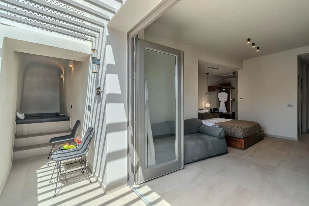 Junior Suite veranda in striped pergola shade, two chairs and a small table, glass doors open to the bedroom